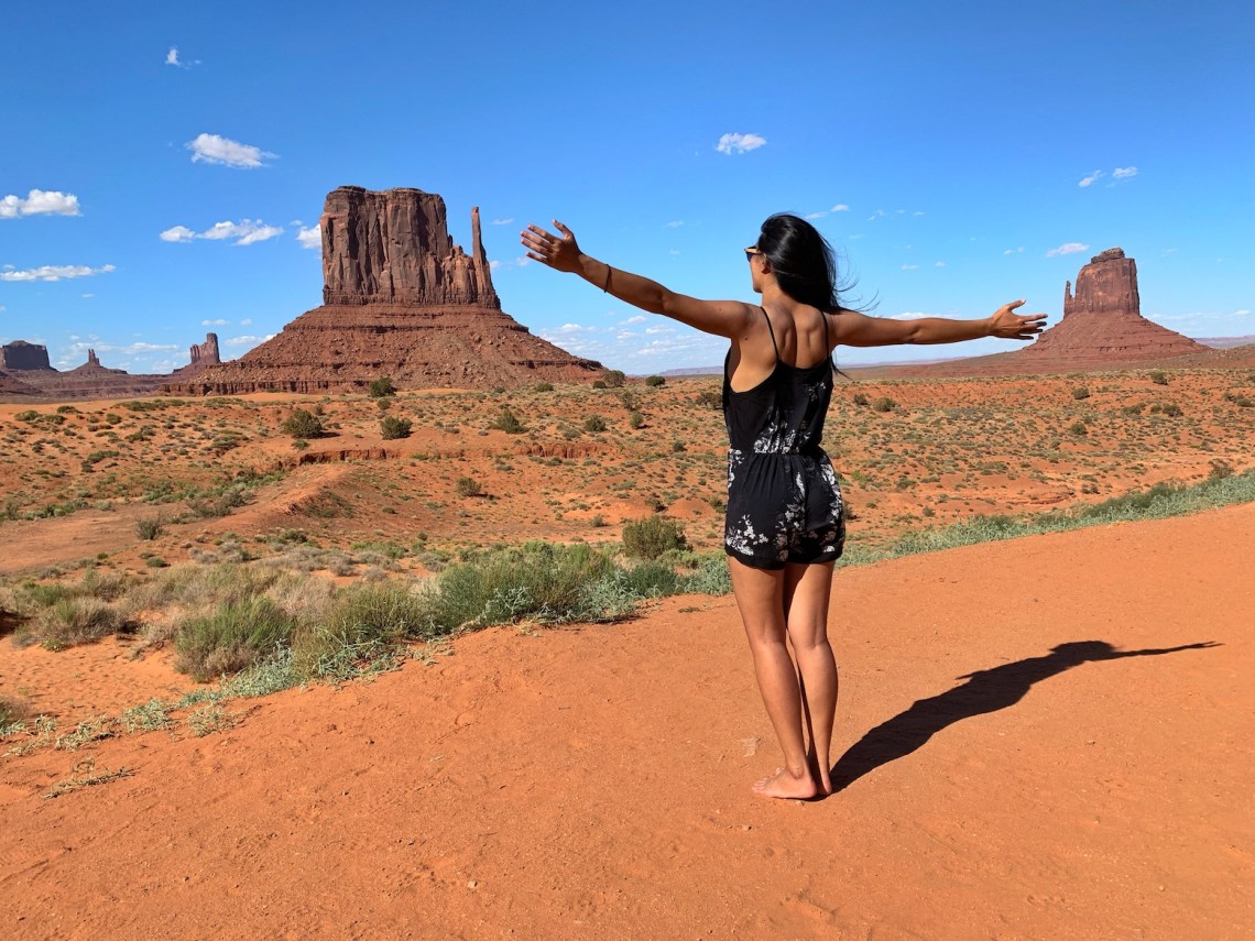 Woman standing in front of Mitton and Merick Buttes in Monument Valley during her USA Roadtrip