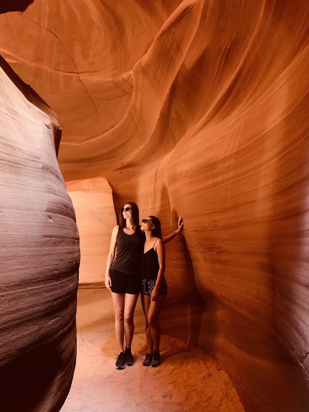 Two woman standing inside Upper Antelope Canyon, surrounded by red sand stone walls