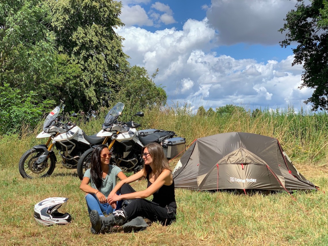 Two motorcyclists sitting in front their ADV Tent in a field and two Tiger 900 Rally Pro motorcycles in the background