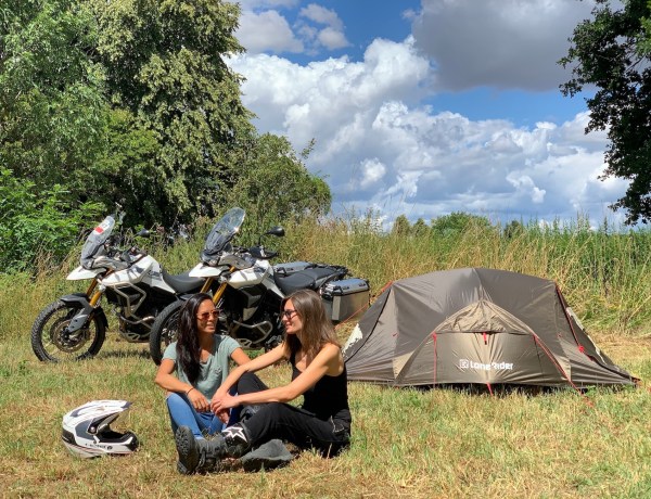 Two motorcyclists sitting in front their ADV Tent in a field and two Tiger 900 Rally Pro motorcycles in the background